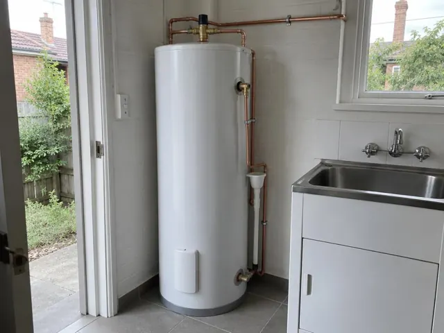 White hot water cylinder with copper pipework beside a laundry sink and tiled wall in a home in Neutral Bay